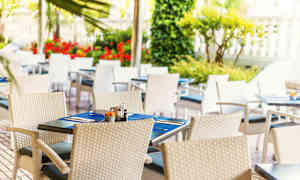 Uteservering med vita flätade stolar och dukade bord med blåa bordstabletter. (AI-genererad text)