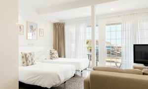 Ett ljust hotellrum med två enkelsängar, stora fönster och havsutsikt. (AI-genererad text)