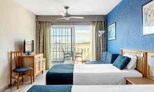 Bild av ett hotellrum med två sängar, en blå vägg och en glasdörr mot en balkong. (AI-genererad text)