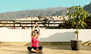 Person sitter i yogaposition på en terrass med utsikt över staden och berg. (AI-genererad text)