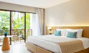 Ett hotellrum med en dubbelsäng, ljusa möbler och en balkong med utsikt mot trädgården. (AI-genererad text)