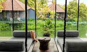 Hängande sittmöbler på en terrass med utsikt över en grönskande trädgård och små hus med tak av brunt trä. (AI-genererad text)