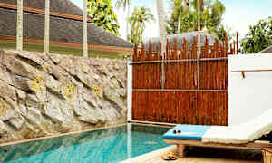 En privat pool med solstol bredvid och stenar pryder väggen bakom poolen. (AI-genererad text)