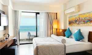 Hotellrum med en stor säng, blå kuddar och havsutsikt från balkongen. (AI-genererad text)