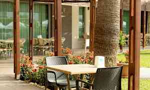 En uteplats med bord, stolar och blommor framför en byggnad med glasfönster. (AI-genererad text)