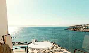 En balkong med utsikt över havet, parasoll vid en pool, och en kopp på ett bord. (AI-genererad text)