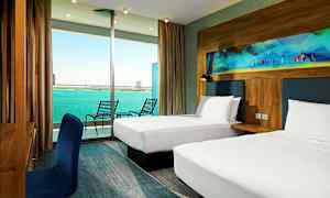 Ett hotellrum med två enkelsängar, ett skrivbord med en blå stol och en balkong med utsikt över havet. (AI-genererad text)