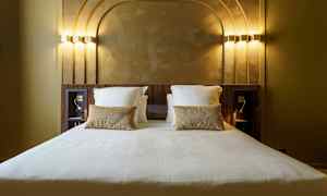 Hotellsäng med vita sängkläder och guldkuddar i ett rum med dekorativt bakstycke. (AI-genererad text)