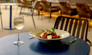 Uteservering vid havet med en tallrik sallad och ett glas vitt vin på ett bord. (AI-genererad text)