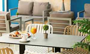 Ett inomhusområde med sittmöbler och ett bord där en frukostservering med juice, kaffe och ägg är framställd. Växter placerade runt omger sittplatserna. (AI-genererad text)