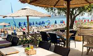 En uteservering med parasoller nära en strand med solstolar och utsikt över havet. (AI-genererad text)