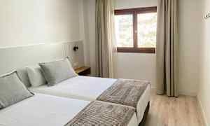 Ett hotellrum med två enkelsängar, ett fönster med ljusinsläpp och del av utsikten utanför. (AI-genererad text)