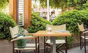 Utomhusmiljö med bord och stolar intill grönska. (AI-genererad text)