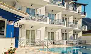 En byggnad med flera våningar, vit fasad och blå detaljer, omgiven av en pool och uteplats. (AI-genererad text)