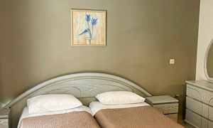 Två enkelsängar med bruna överkast, en målning på väggen ovanför och en byrå till höger. (AI-genererad text)