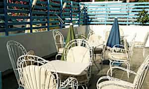 En terrass med vita trädgårdsstolar och bord, omgiven av en blåmålad spaljé och blommande buskar. (AI-genererad text)