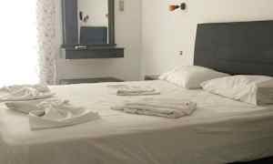 Ett sovrum med en dubbelsäng, sängkläder skymt på sängen. En spegel hänger på väggen bredvid. (AI-genererad text)