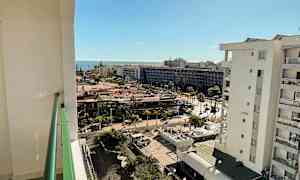 Utsikt från en balkong över ett stadslikt område och havet i bakgrunden, med soligt väder. (AI-genererad text)