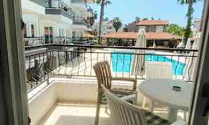 Utsikt från en balkong över ett poolområde och anslutande byggnader. (AI-genererad text)