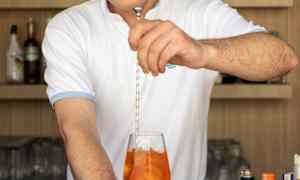 En bartender blandar en drink med orange vätska i ett vinglas. (AI-genererad text)