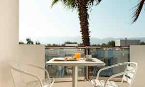 En balkong med ett bord, två vita stolar och frukost serverad. En palm ses i bakgrunden. (AI-genererad text)