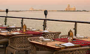 En utomhusrestaurang med dukade bord och utsikt över havet vid solnedgången. (AI-genererad text)