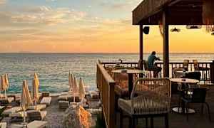 En solnedgång vid havet med en restaurangterrass och solstolar på stranden. (AI-genererad text)