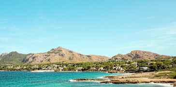 Kustlinje med klarblått vatten och berg i bakgrunden. (AI-genererad text)