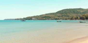 En strand med klart vatten och båtar längre ut på havet. (AI-genererad text)