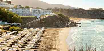 Strand med solstolar och parasoller, byggnader på sluttningen. (AI-genererad text)