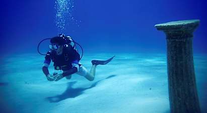 En dykare under vatten nära en antik pelare på havsbotten. (AI-genererad text)