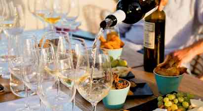 Ett bord med glas fyllda med vitt vin som serveras, omgivna av olika tilltugg som ost, bröd och frukt. (AI-genererad text)