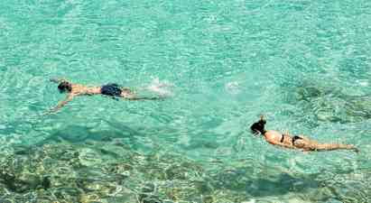 Två personer snorklar i klart turkost vatten. (AI-genererad text)