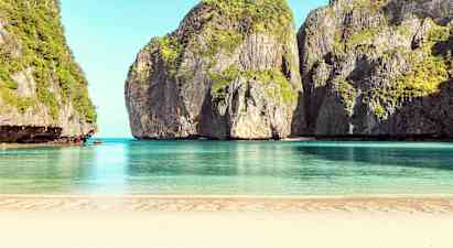 En sandstrand som vetter mot lugnt blått vatten, omgiven av höga klippor täckta av vegetation. (AI-genererad text)