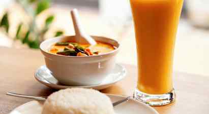 En skål med gul curry, en tallrik med ris och ett glas med gul dryck. (AI-genererad text)