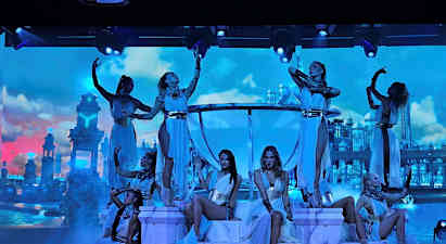 Dansare poserar på en upplyst scen med en dekor av palatsliknande byggnader mot en molnig himmel. (AI-genererad text)