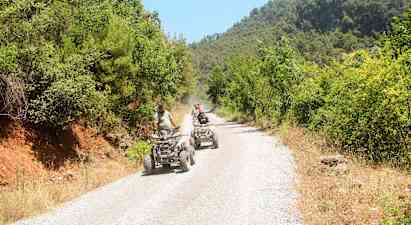 Personer kör fyrhjulingar på en grusväg omgivet av grönska. (AI-genererad text)