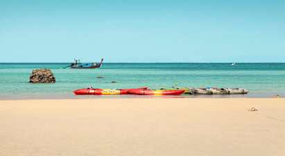 Flera kajaker på en sandstrand, med havet och en båt i bakgrunden. (AI-genererad text)