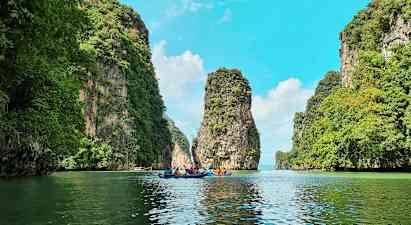 Flera personer paddlar kajaker genom en naturskön passage mellan höga, gröna klippor. (AI-genererad text)