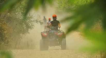 Personer som kör fyrhjulingar på en dammig grusväg omgiven av växtlighet. (AI-genererad text)