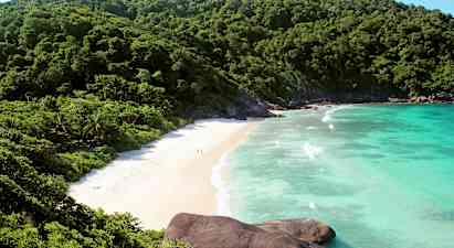 Bild på en strand omgiven av gröna berg och blått hav. (AI-genererad text)