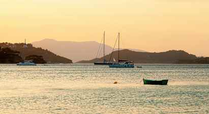 Bild av en stilla vik vid solnedgången med segelbåtar och en grön båt i förgrunden. (AI-genererad text)