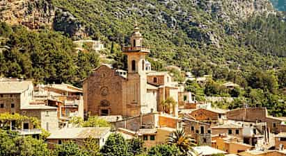 Stenkyrka med torn omgiven av en by bland berg och grönska. (AI-genererad text)