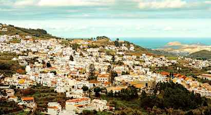 Vy över en stad med många vita byggnader som ligger i en grönskande dal nära havet. (AI-genererad text)