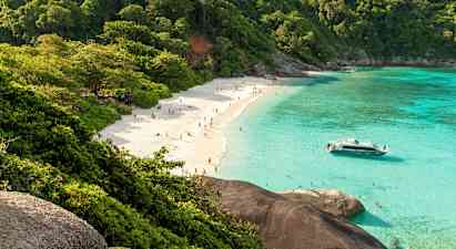 En sandstrand med människor, omgiven av grönskande träd och klart turkost vatten. En båt ligger nära stranden. (AI-genererad text)