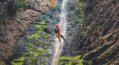 Person som firar sig ner för ett vattenfall med rep, omgivna av klippor och vegetation. (AI-genererad text)