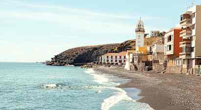 Bild på en kust med svarta sandstränder, en fyr och byggnader vid vattenkanten. (AI-genererad text)