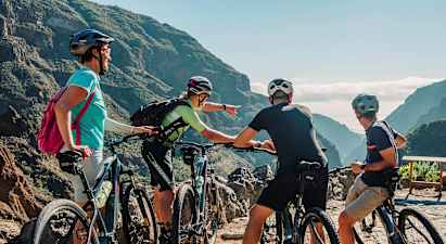 En grupp människor med mountainbikes tittar på en naturskön utsikt mellan berg med grönskande dalar. (AI-genererad text)