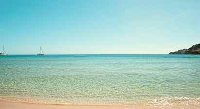 Strand med klart vatten och två segelbåtar i havet. (AI-genererad text)