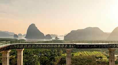 En bro med pelare leder till ett område med vatten och berg i bakgrunden. (AI-genererad text)